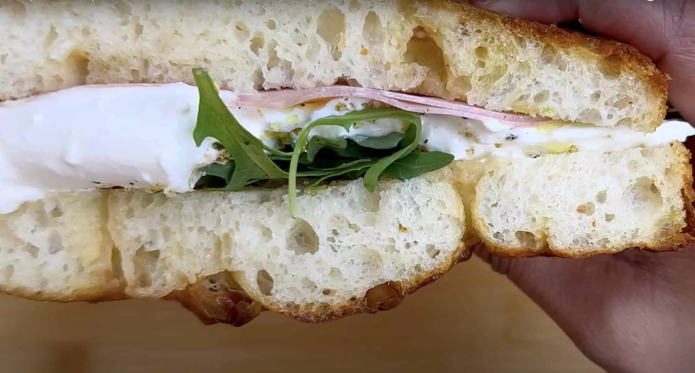 Close-up of a fresh sandwich with arugula, ham, cheese, and rustic bread, perfect for a quick, delicious meal.